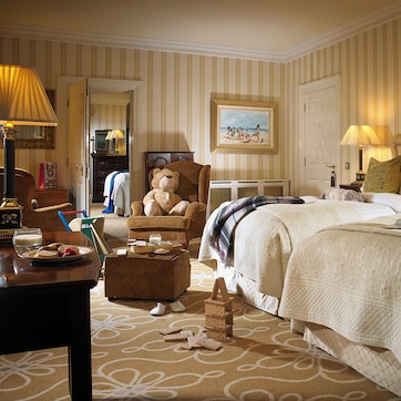 A hotel room with a large bed, a sitting area with a chair and a table, a dresser, a mirror, and a painting on the wall.