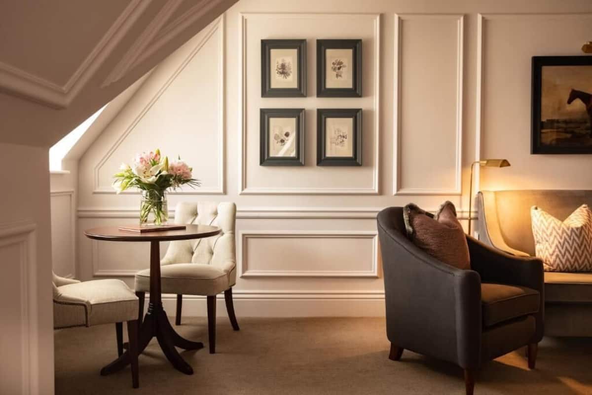 A room with a dining table, two chairs, a sofa, and framed artwork on the wall.