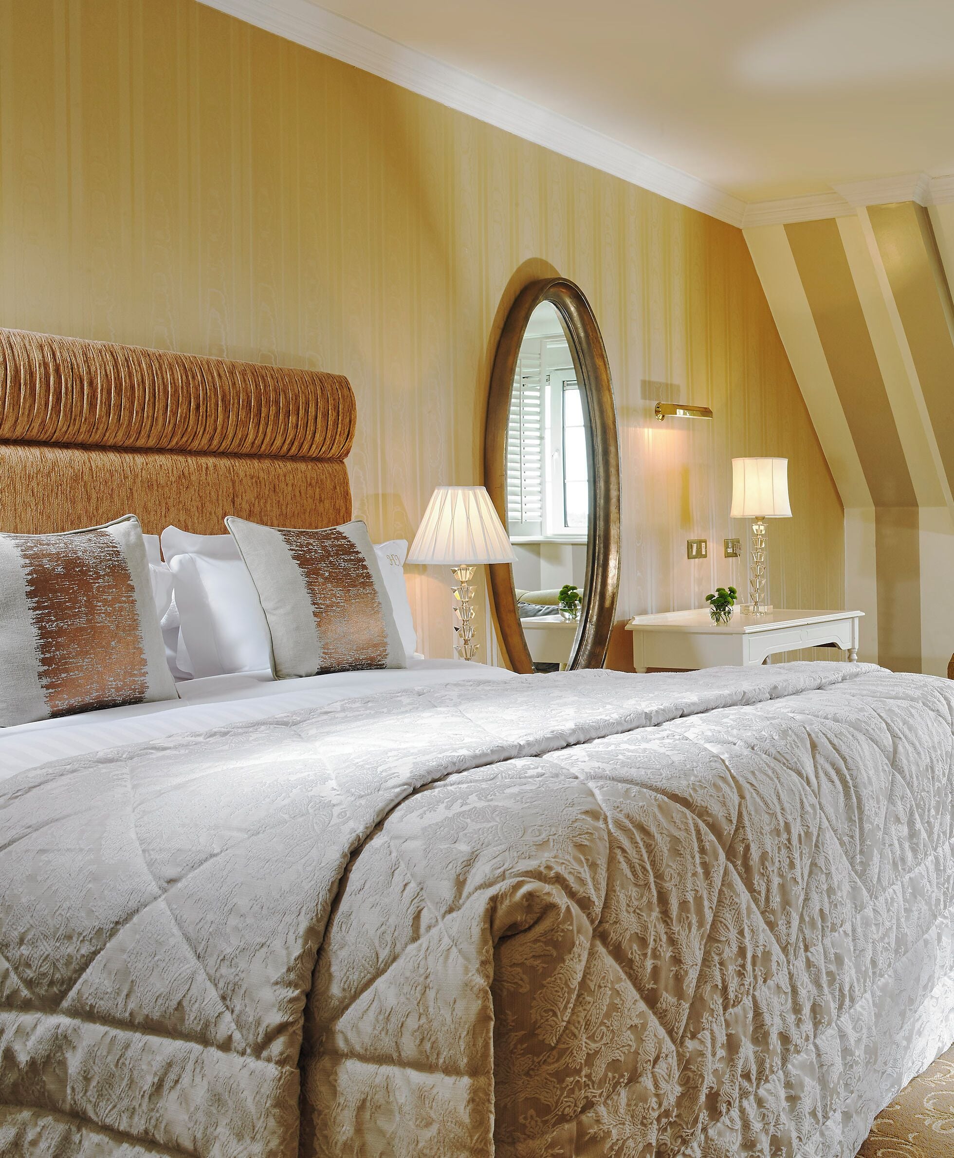A bedroom with a large bed, a mirror, a bedside table, and a lamp.