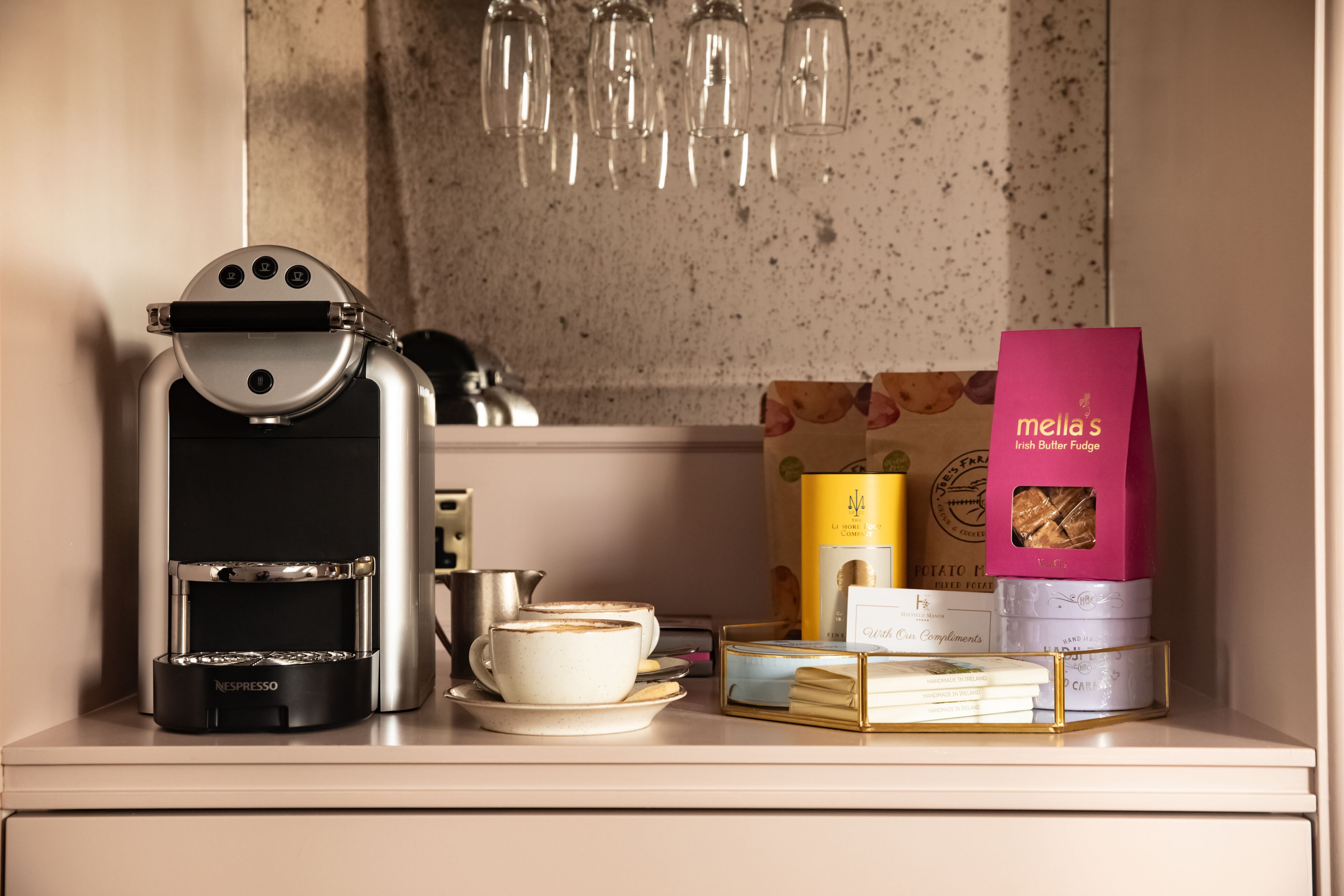A coffee machine, a cup, a box of Mella's Irish Butter Fudge, and a stack of books on a counter.