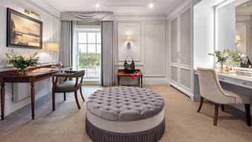 Une chambre d’hôtel avec un pouf rond, un bureau avec une chaise, un grand miroir et une vue sur l’extérieur.