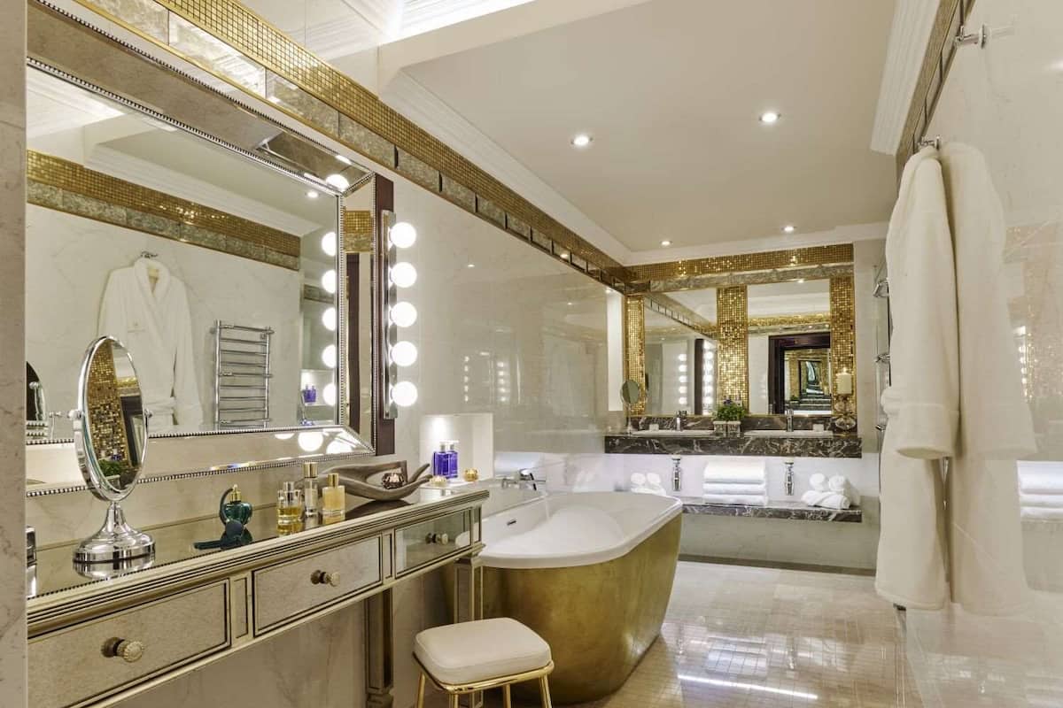 A luxurious bathroom with a large vanity, a freestanding bathtub, and multiple mirrors with lights.