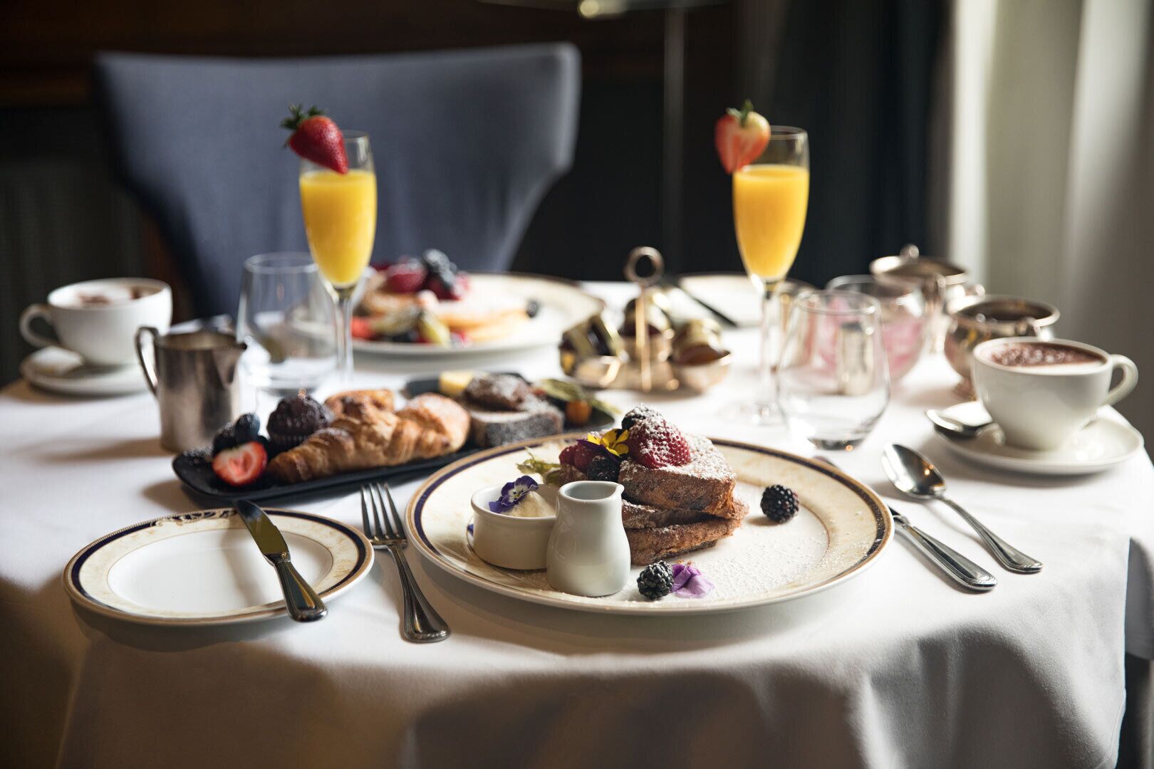 A breakfast setting with plates of pastries, fruits, and beverages on a table.