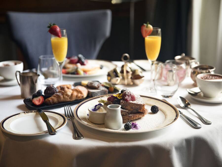 Desayuno con platos de pasteles, frutas y bebidas sobre una mesa.