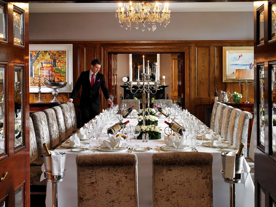 A formal dining room with a long table set for a banquet, a chandelier, and wooden paneling.