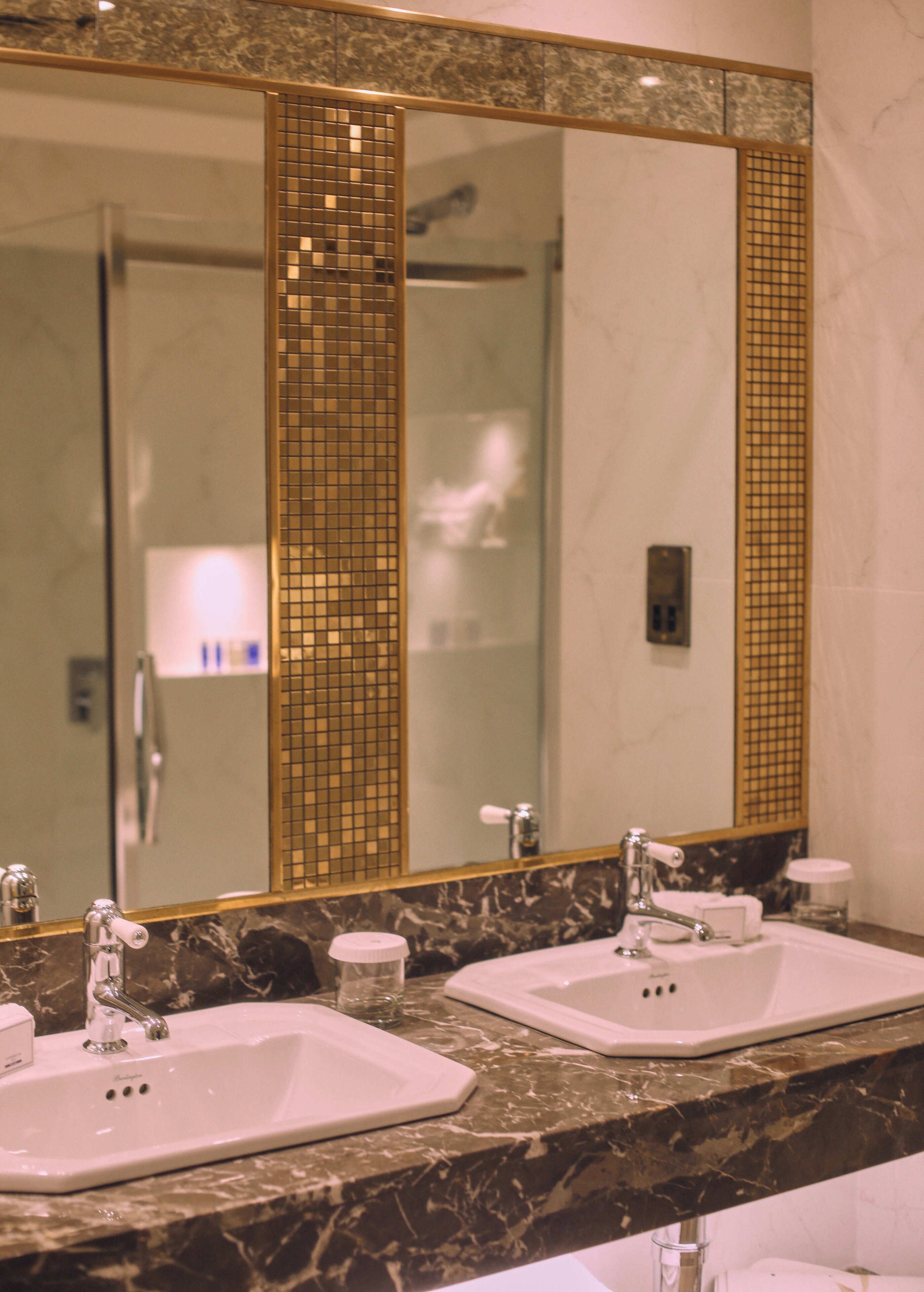 A bathroom with two sinks, a large mirror, and a shower visible in the background.