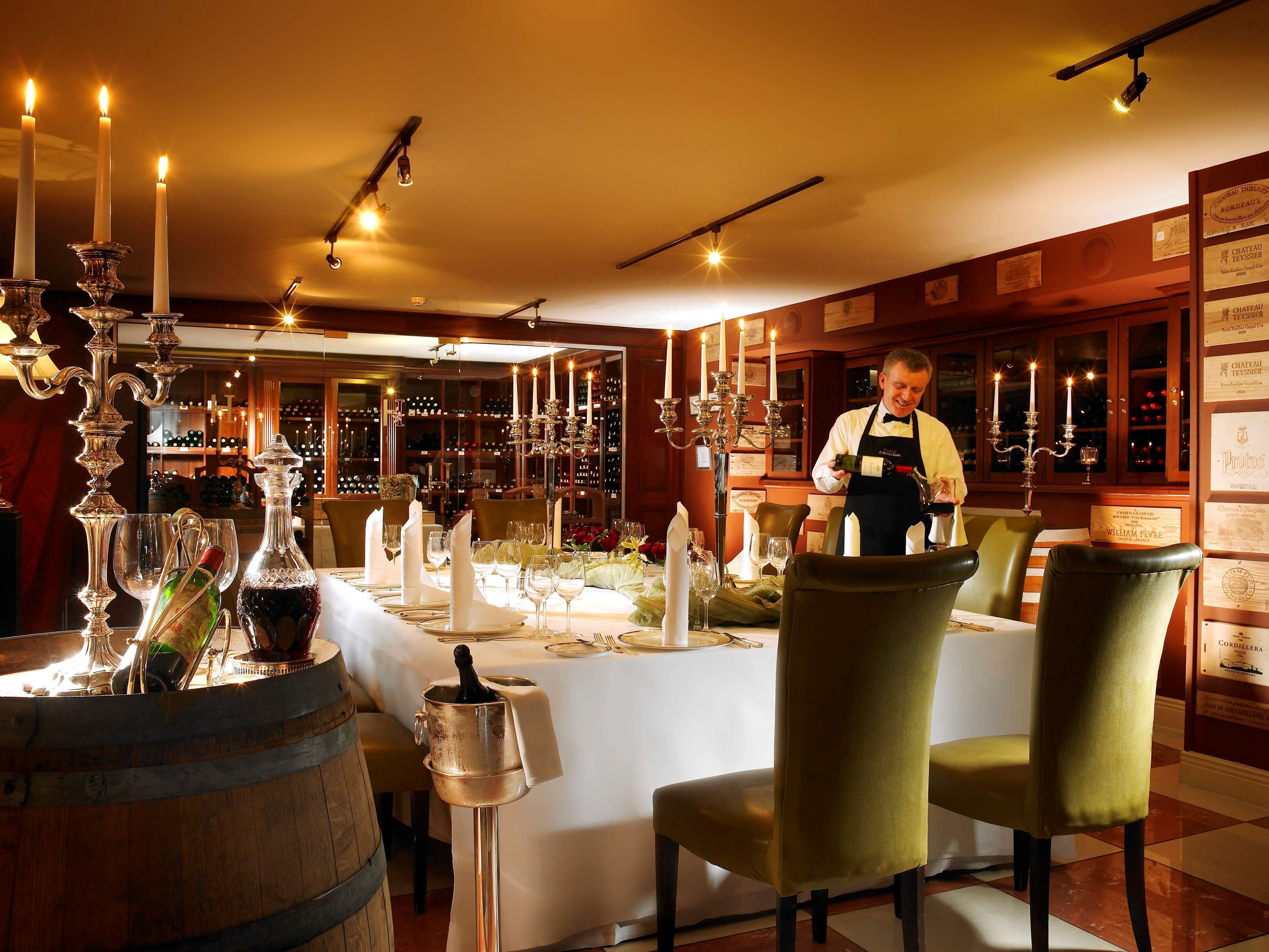 A restaurant with a long table set for dining, candles, and a wine bottle on a stand.