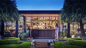 An outdoor bar area with a stone facade, a bartender, and guests seated at tables. - Hayfield Manor (Cork)