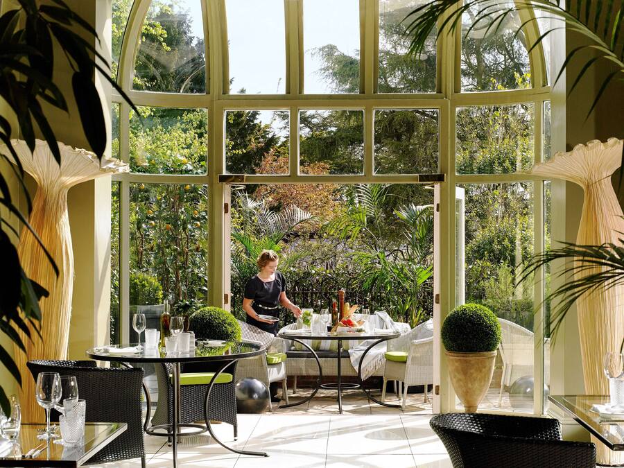 A conservatory with a chef preparing food, dining tables, and chairs.