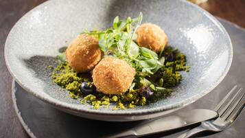 A plate with three round, golden-brown fried balls, green leafy garnish, and a scattering of green crushed nuts.