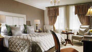 A neatly arranged bedroom with a large bed, a chair, a table with a lamp, and curtains.