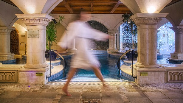 Un área de piscina interior con columnas de piedra, piso de baldosas y techo abovedado.