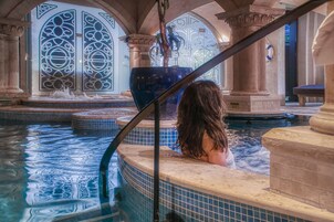 Una persona en un jacuzzi con un ventanal decorativo grande y columnas al fondo.
