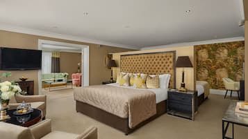 Amplia habitación de hotel con una cama grande, televisión de pantalla plana, comedor con mesa y sillas, y un elemento decorativo en la pared.