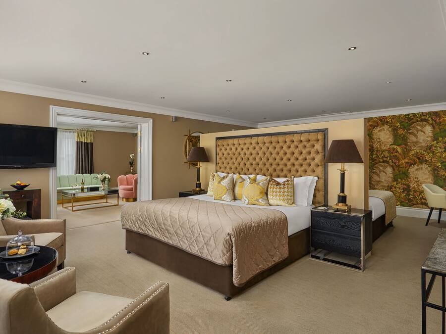 Amplia habitación de hotel con una cama grande, televisión de pantalla plana, comedor con mesa y sillas, y un elemento decorativo en la pared.