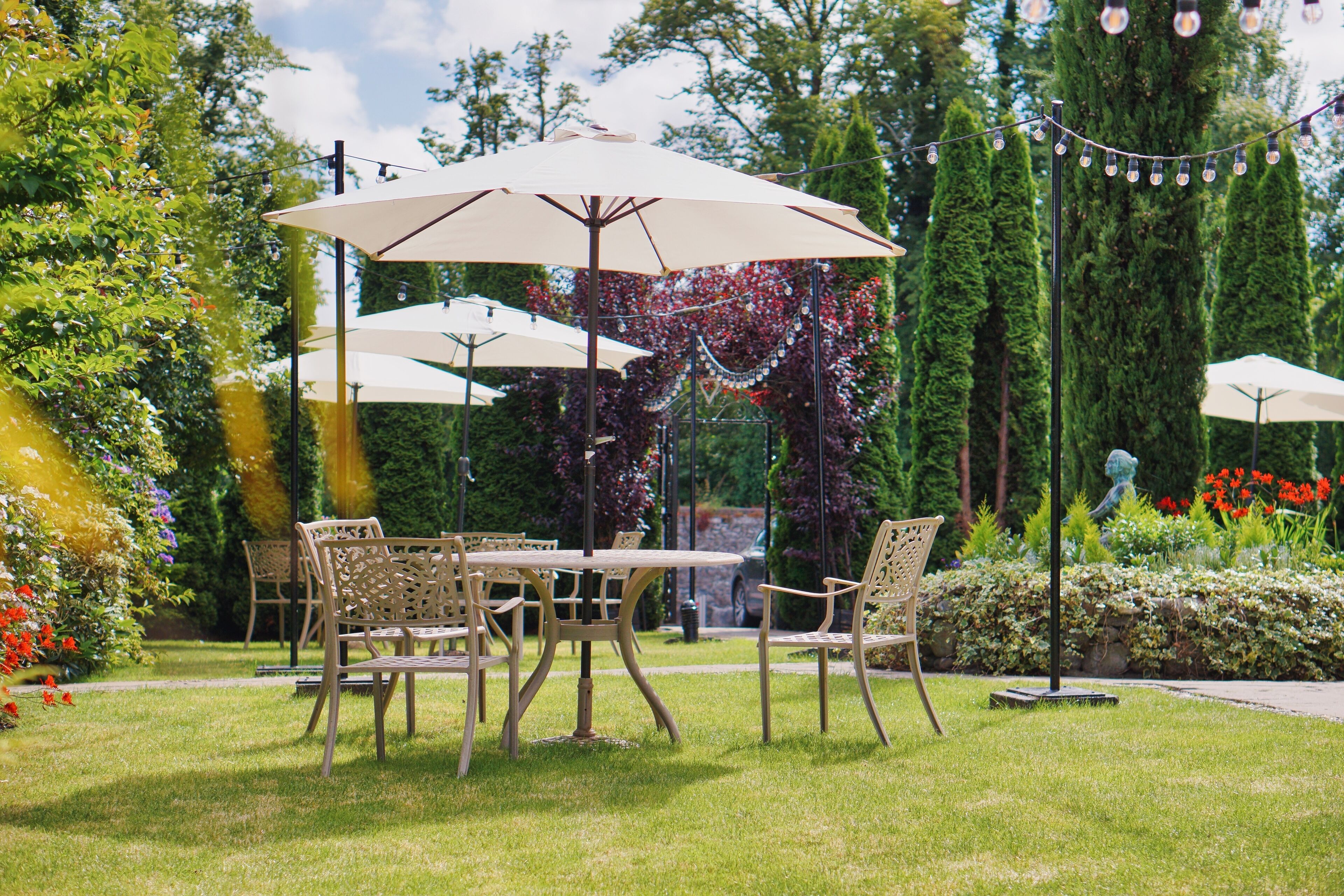 Un espace extérieur aménagé avec des tables et des chaises, entouré d’une végétation luxuriante et illuminé de guirlandes décoratives.