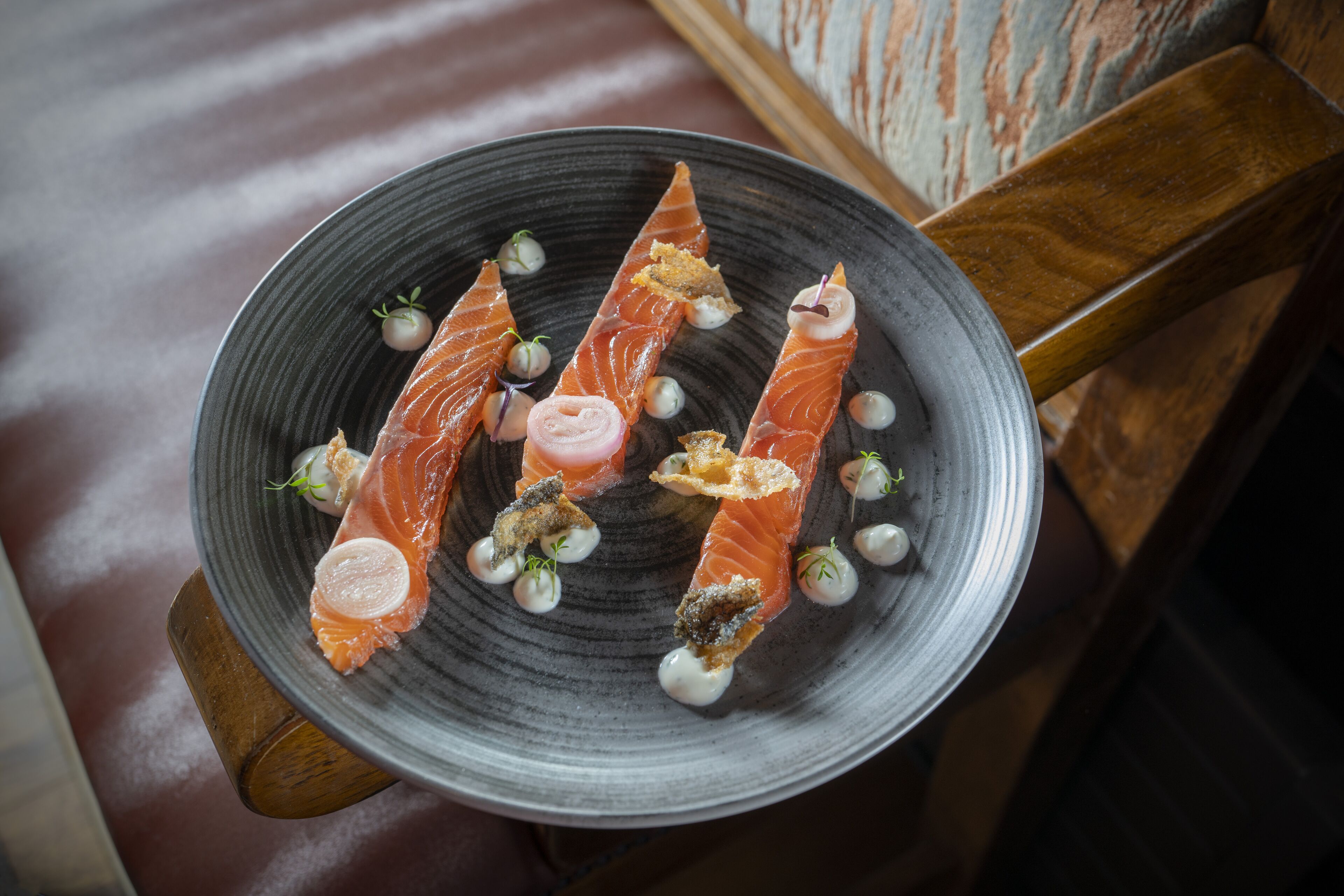 A plate of salmon with garnishes and a wooden chair in the background.