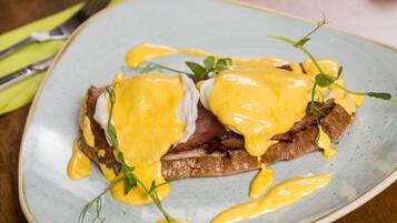Un plato de comida con huevos benedictinos y tocino sobre tostada, adornado con hierbas.