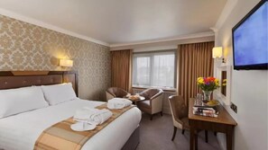 A hotel room with a bed, a desk with a chair, a TV, and a window with curtains.