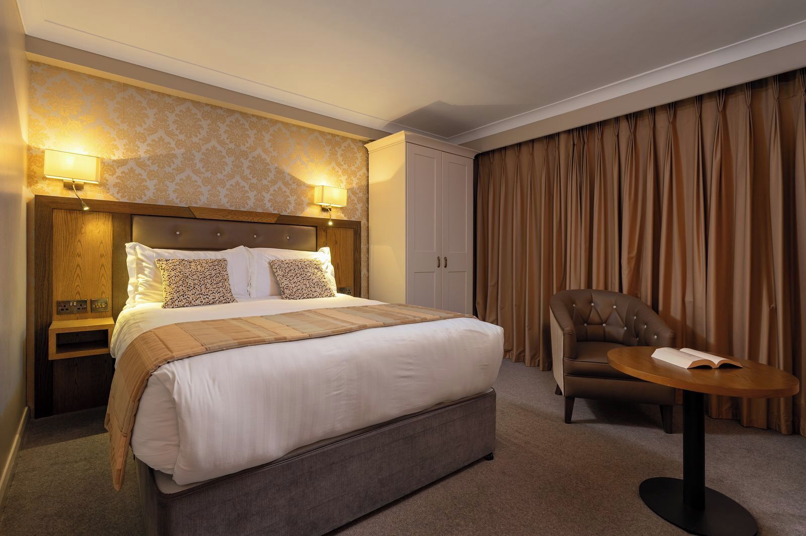 Ein Hotelzimmer mit einem großen Bett, einem Sessel, einem kleinen Tisch und einer Lampe.