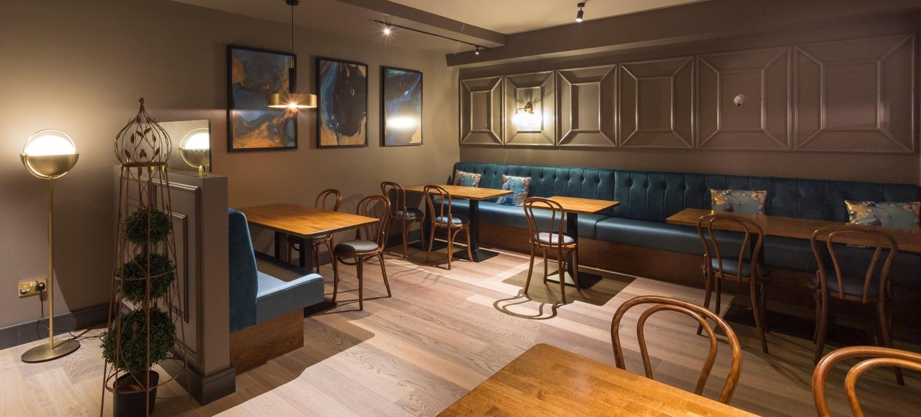 A modern restaurant with a blue upholstered bench, wooden tables, and chairs.