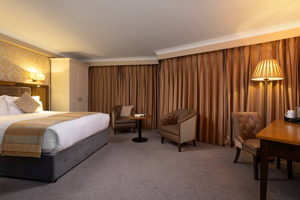 A hotel room with a bed, two armchairs, a small table, and a lamp.