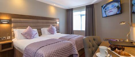 Een hotelkamer met twee bedden, een bureau met een laptop, een kop koffie en een croissant.