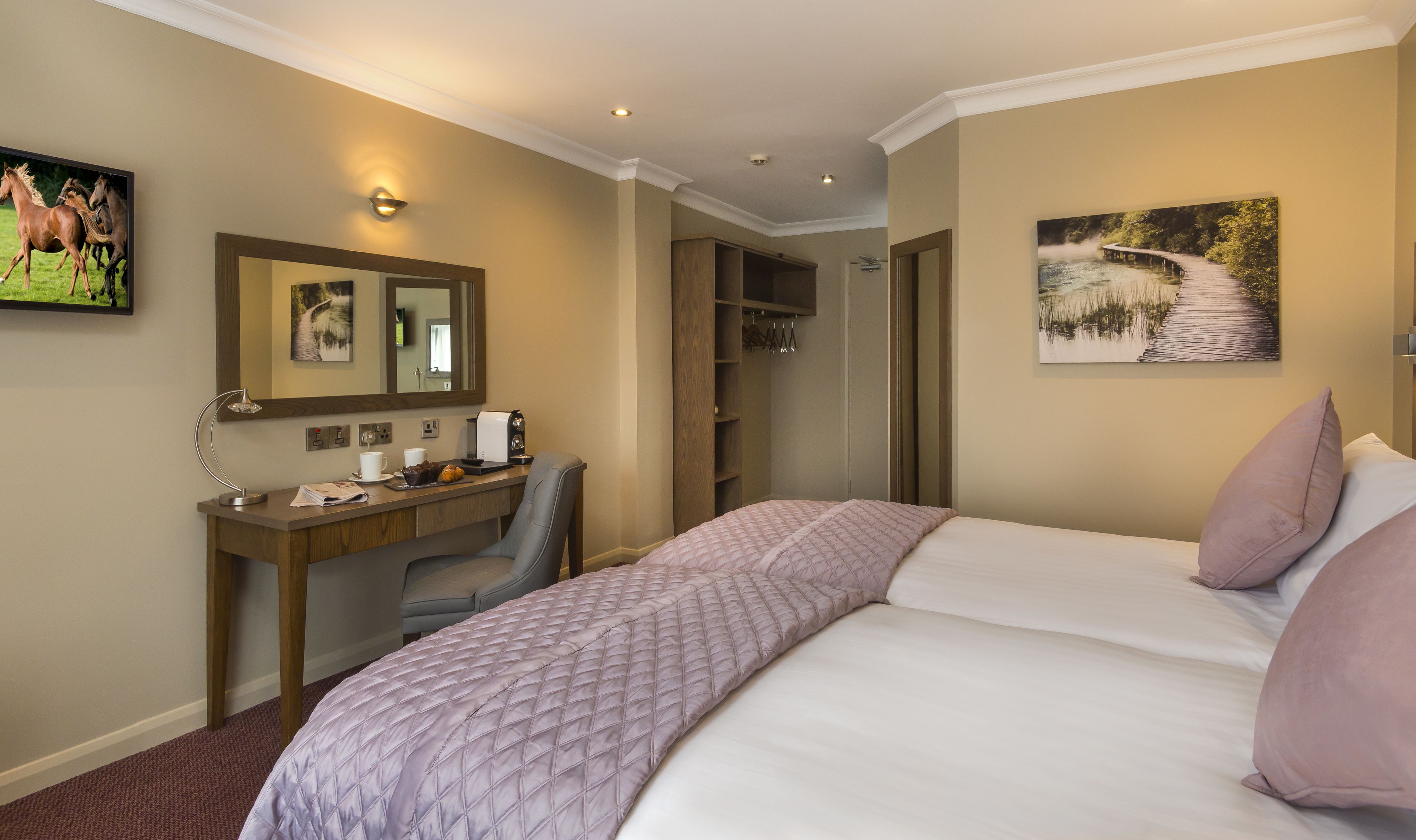 Une chambre d’hôtel comprenant un lit, un bureau avec une machine à café, une chaise, un miroir et des œuvres d’art accrochées aux murs.