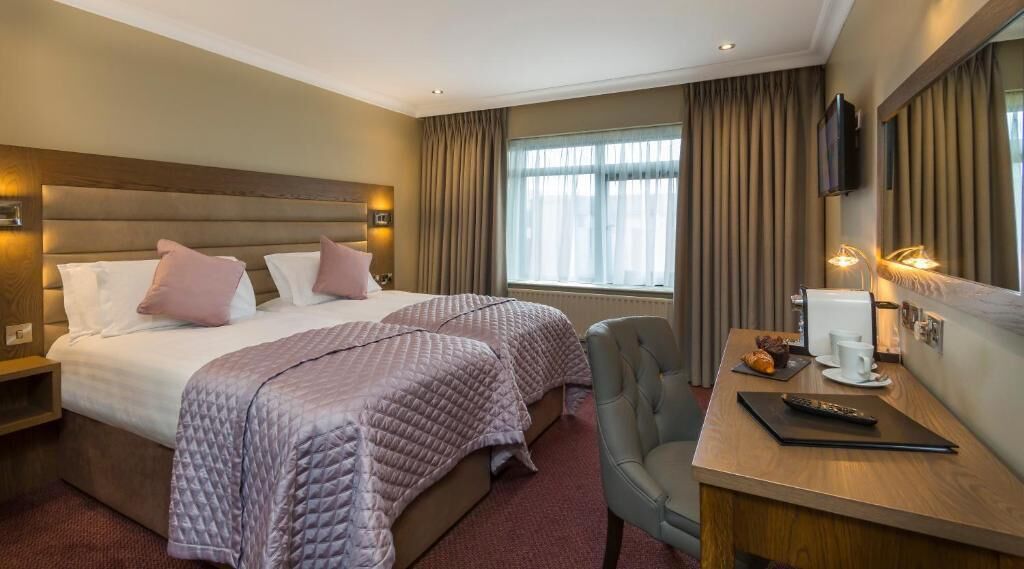 Ein Hotelzimmer mit zwei Betten, einem Schreibtisch mit Stuhl, einem Fernseher und einem Fenster mit Vorhängen.