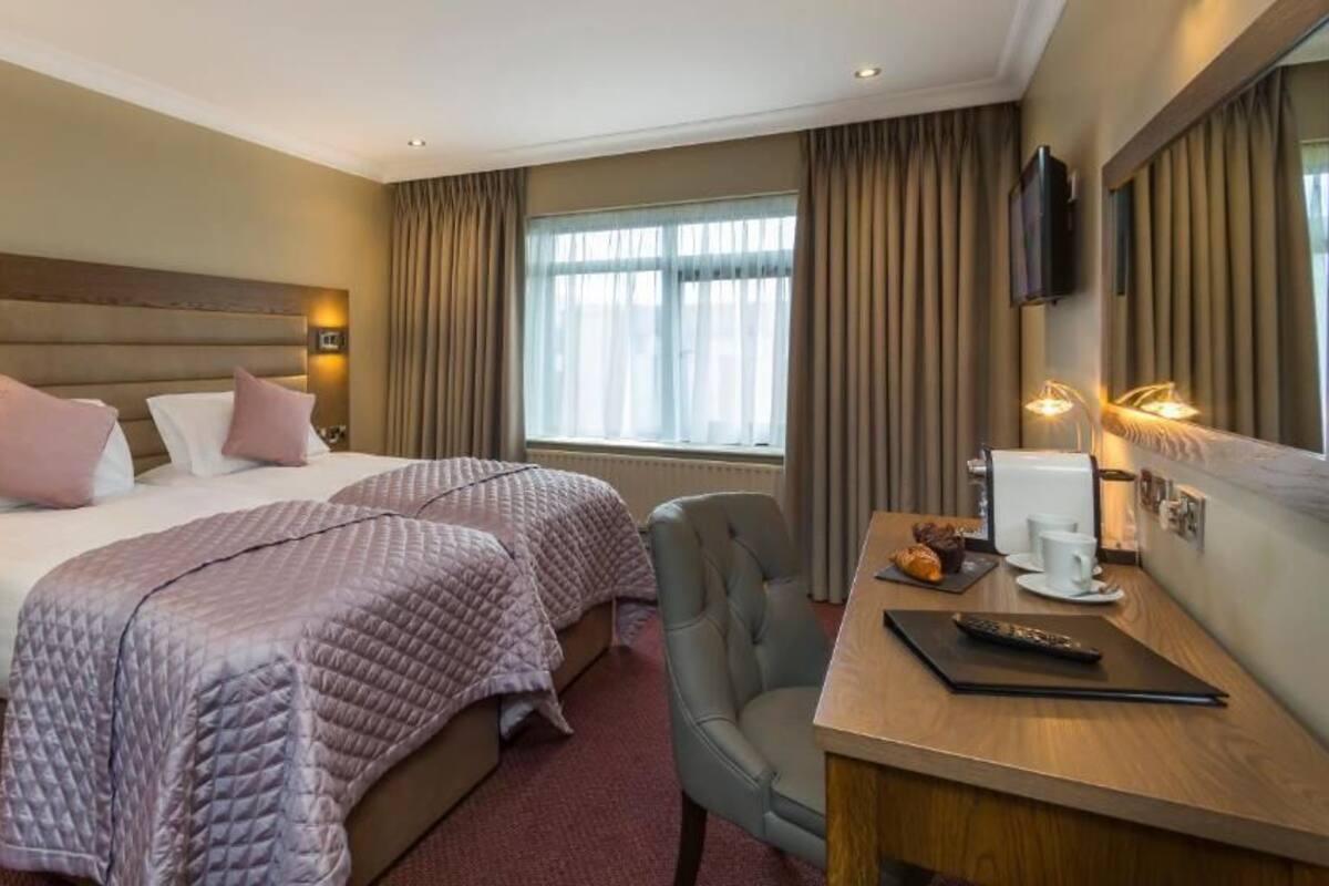 Ein Hotelzimmer mit zwei Betten, einem Schreibtisch mit Stuhl, einem Fernseher und einem Fenster mit Vorhängen.