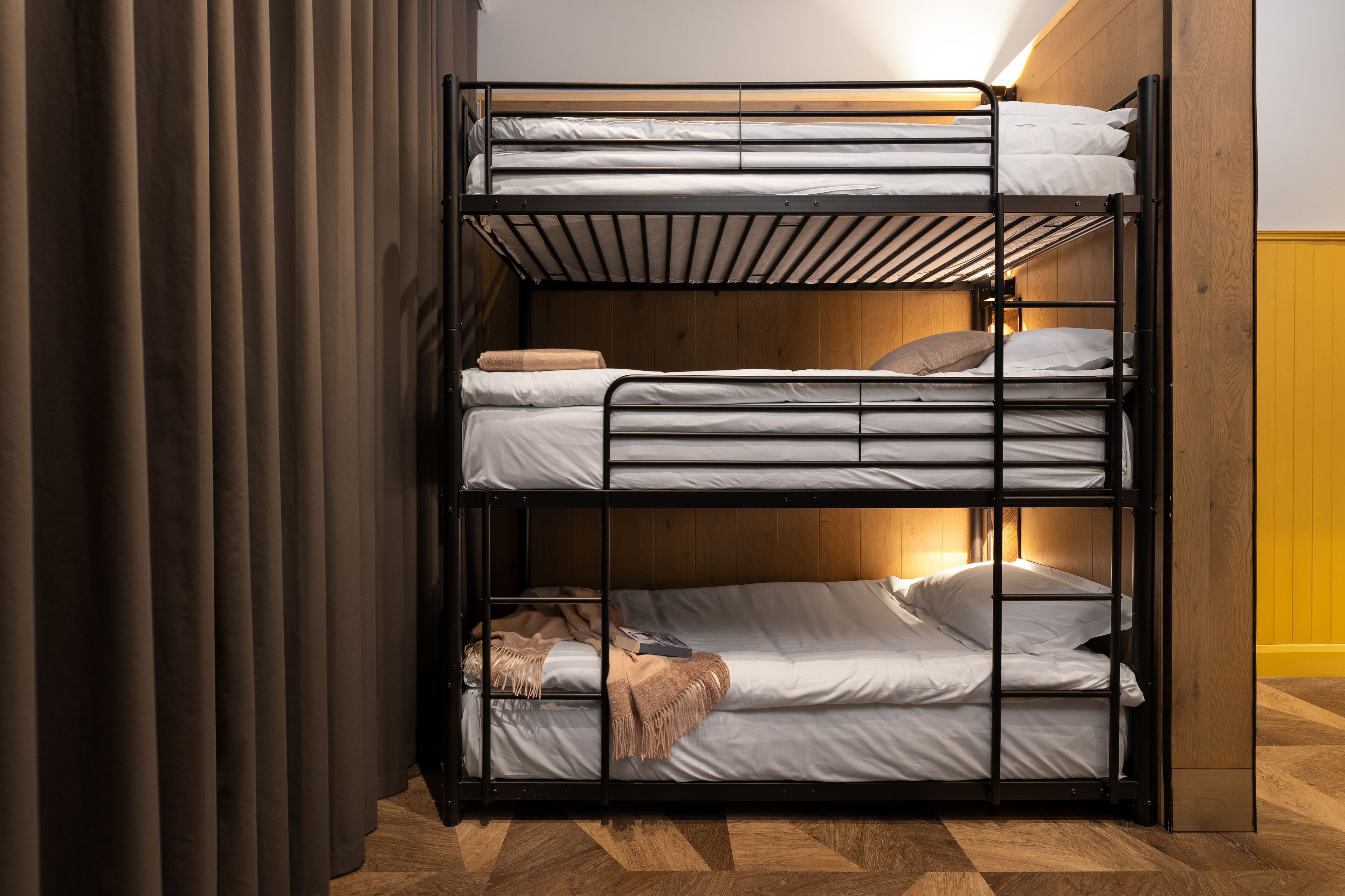 A bunk bed with three levels, wooden walls, and a curtain on the left.