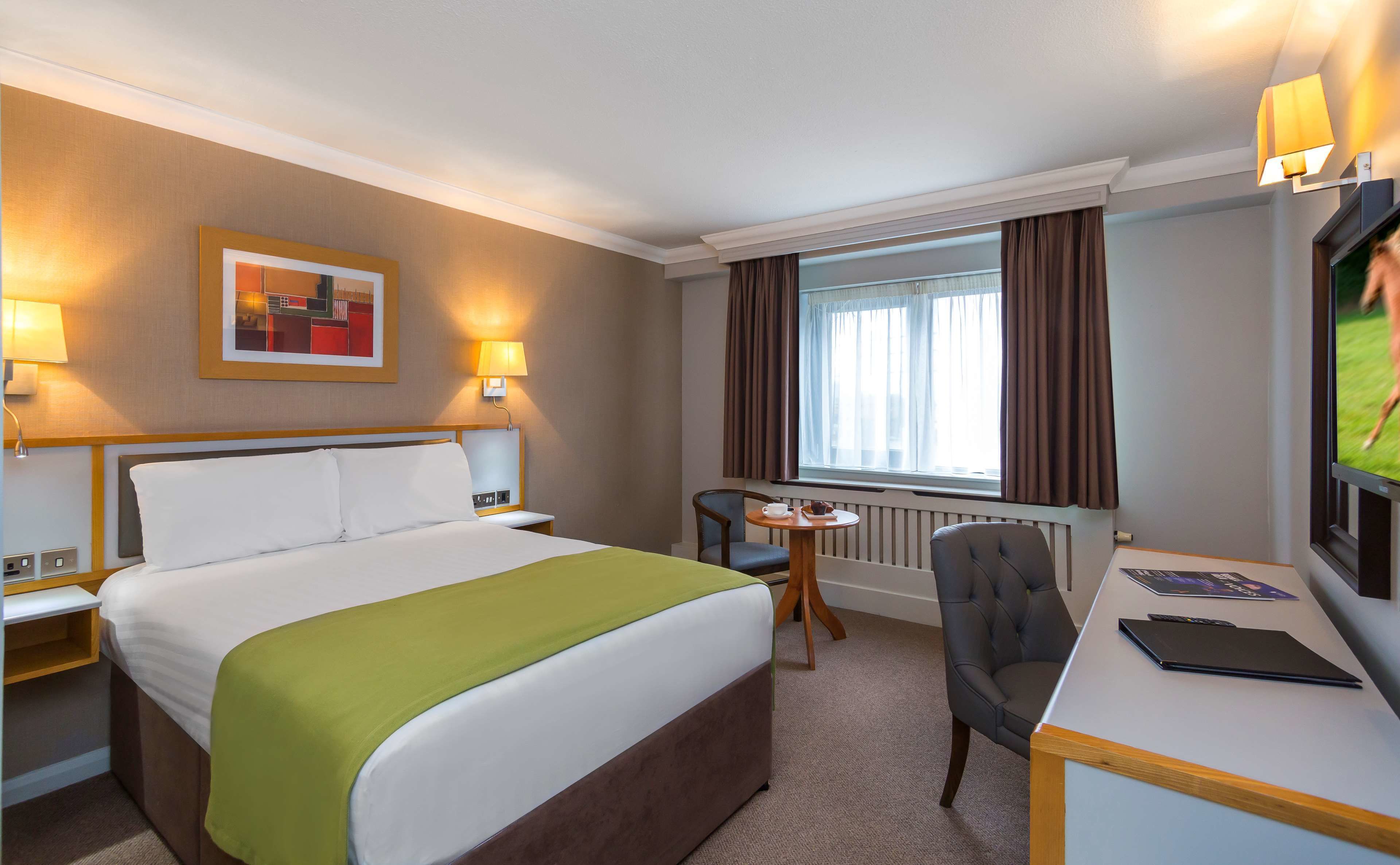 A hotel room with a large bed, a desk, a chair, a television, and a window with curtains.
