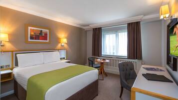 A hotel room with a large bed, a desk, a chair, a television, and a window with curtains.