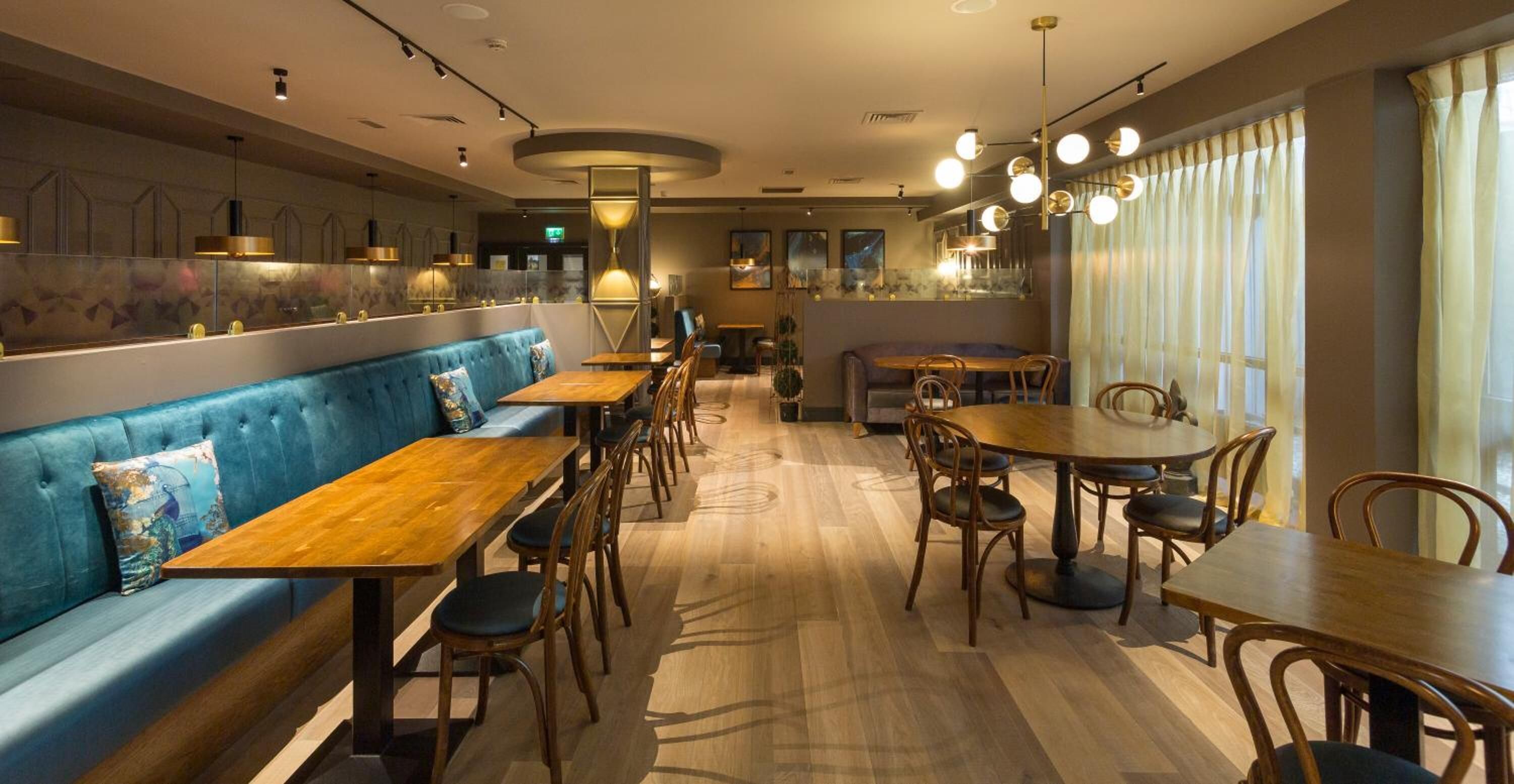 A restaurant with wooden tables and chairs, a blue cushioned bench, and pendant lighting.