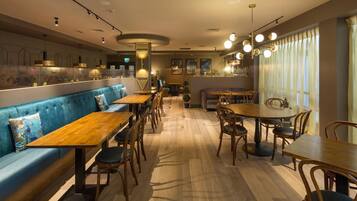 A restaurant with wooden tables and chairs, a blue cushioned bench, and pendant lighting.