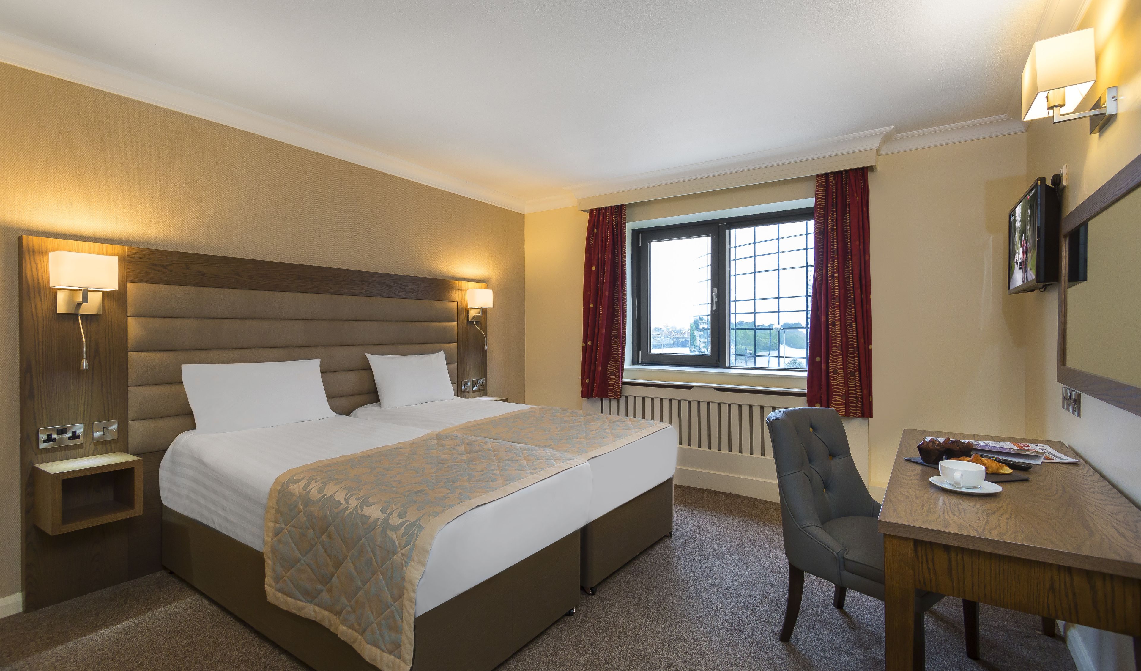 A hotel room with a large bed, bedside tables, a desk, and a window with curtains.