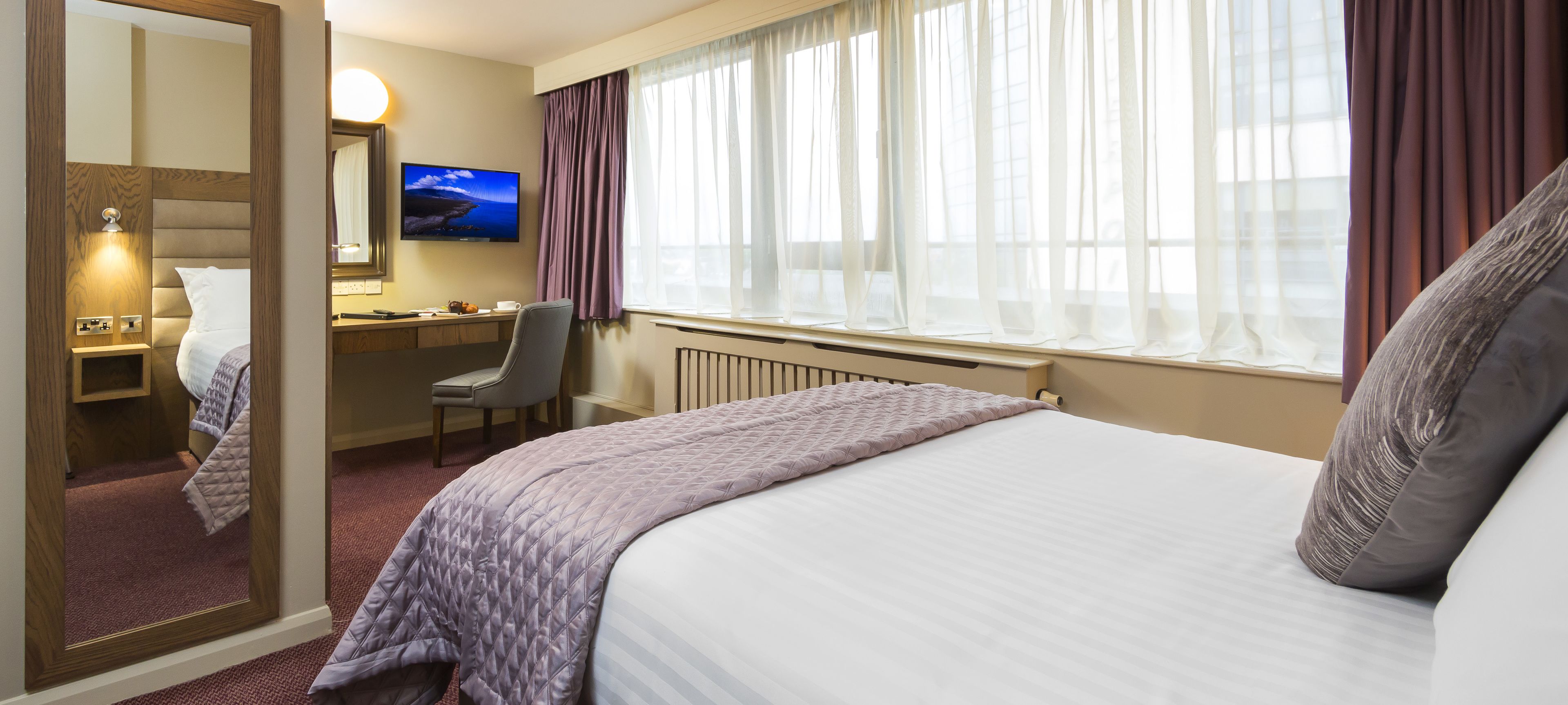 A hotel room with a bed, a desk, a chair, a television, and a window with curtains.