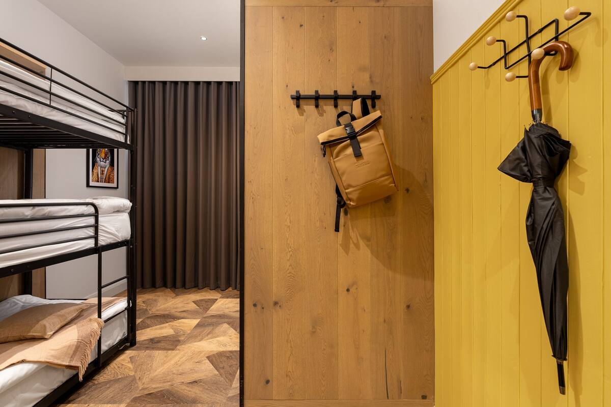 A bunk bed with a wooden floor, a wooden door, and a coat rack with a bag and umbrella.