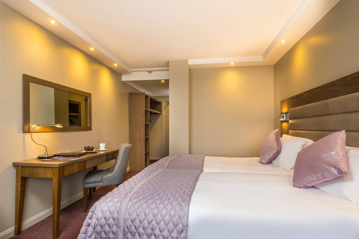 A hotel room with a bed, a desk, a chair, a mirror, and a closet.