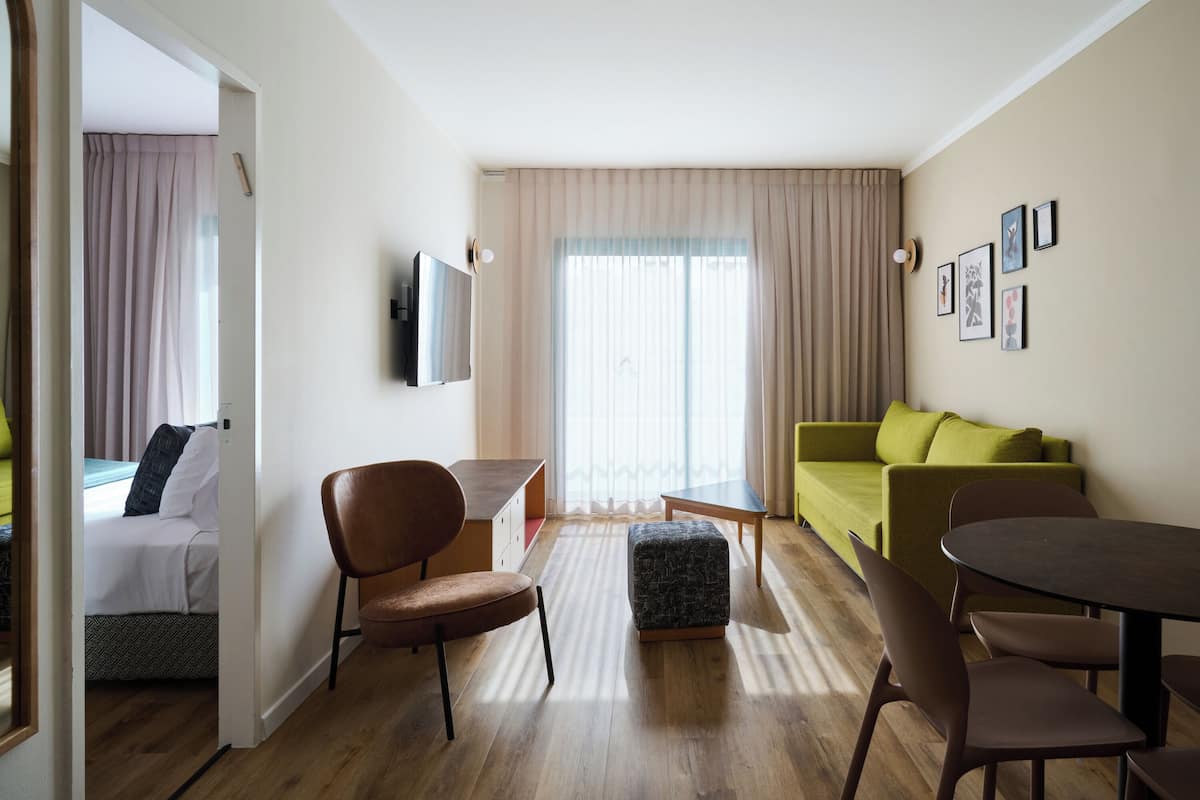 A modern hotel room with a bed, a desk, a green sofa, and a dining table.