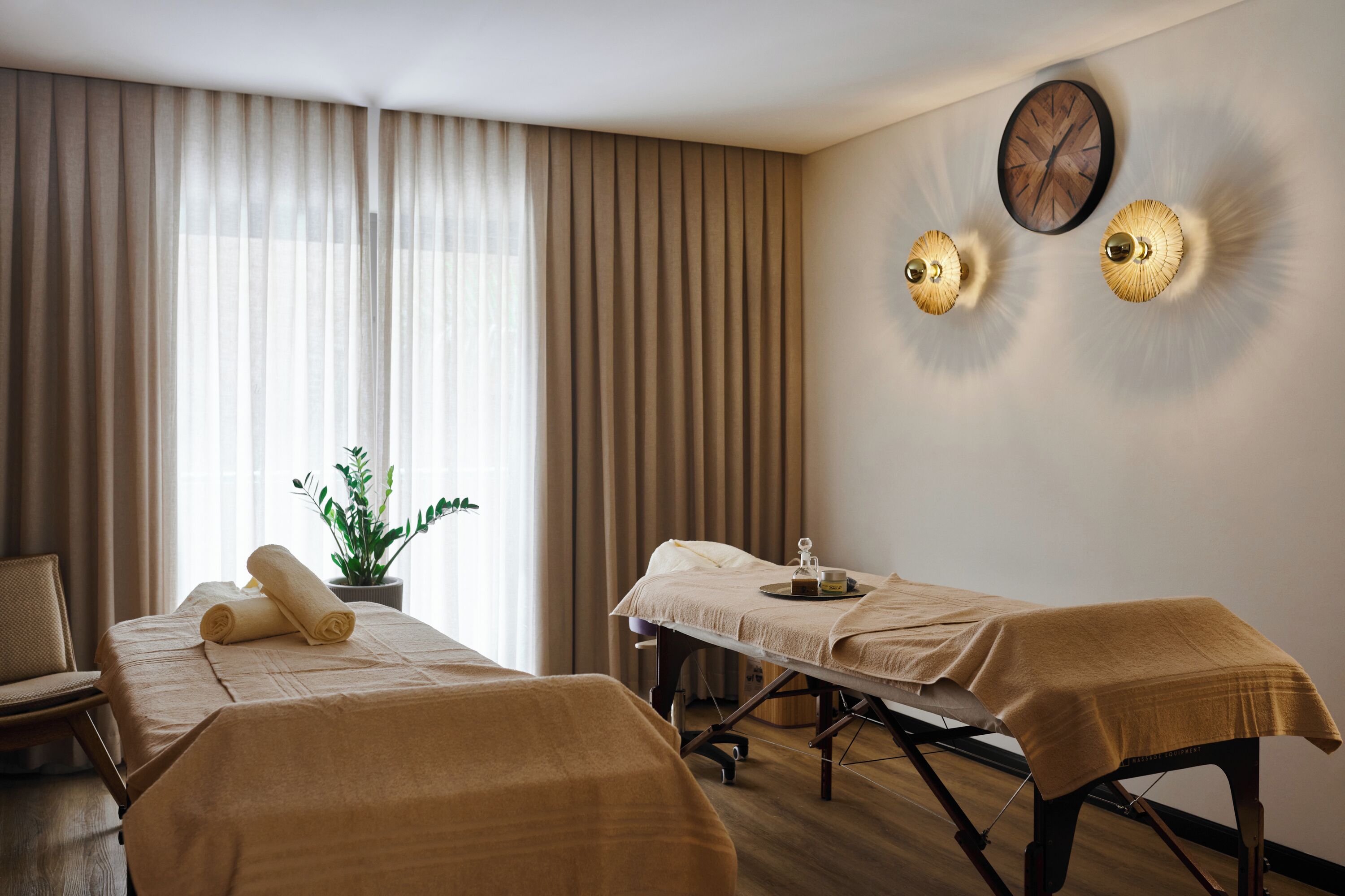 A room with two beds, a potted plant, and a wall clock.