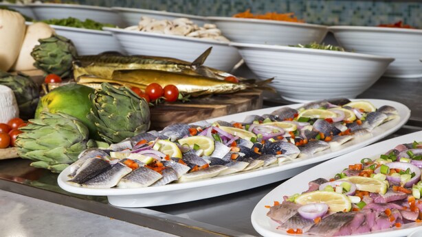 Un bufé con diversos platos, incluyendo pescado, verduras y alcachofas.