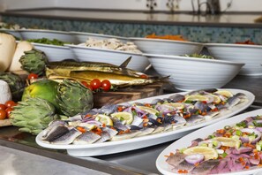A buffet with various dishes including fish, vegetables, and artichokes.