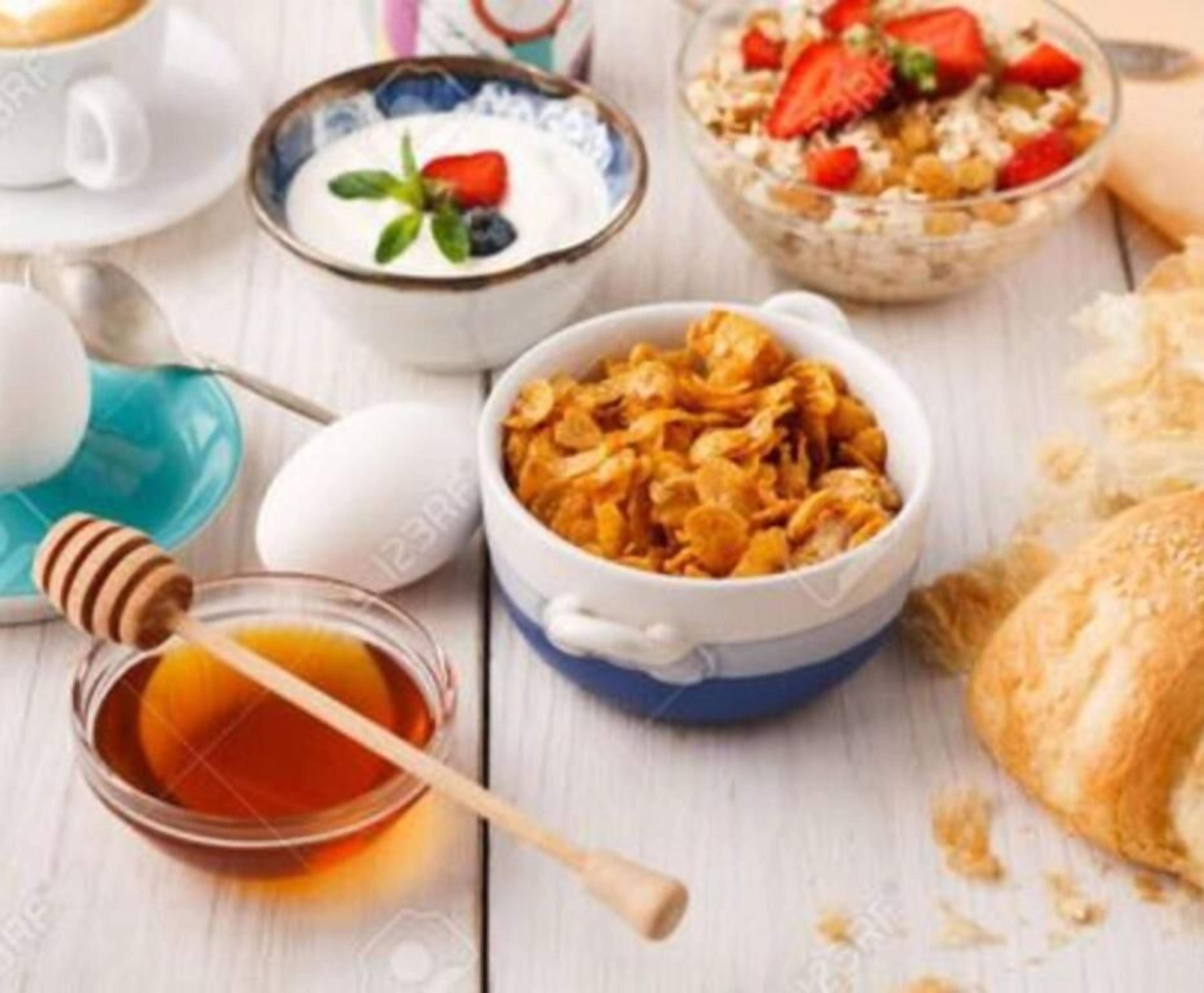 A breakfast setting with cereal, yogurt, strawberries, honey, and a croissant.