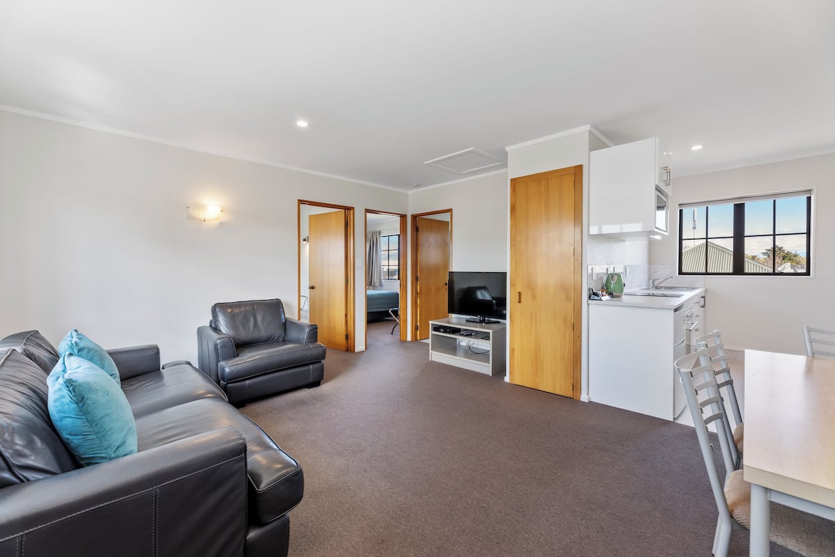 A modern living room with a leather sofa, a TV, and a dining area with a table and chairs.