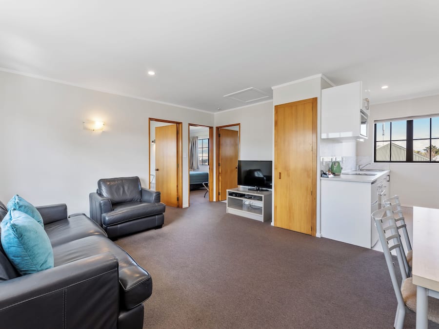 A modern living room with a leather sofa, a TV, and a dining area with a table and chairs.