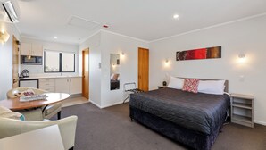 Et moderne hotelværelse med en seng, et sengebord og et lille skrivebord. Der er et tekøkken med en mikrobølgeovn og en vask.