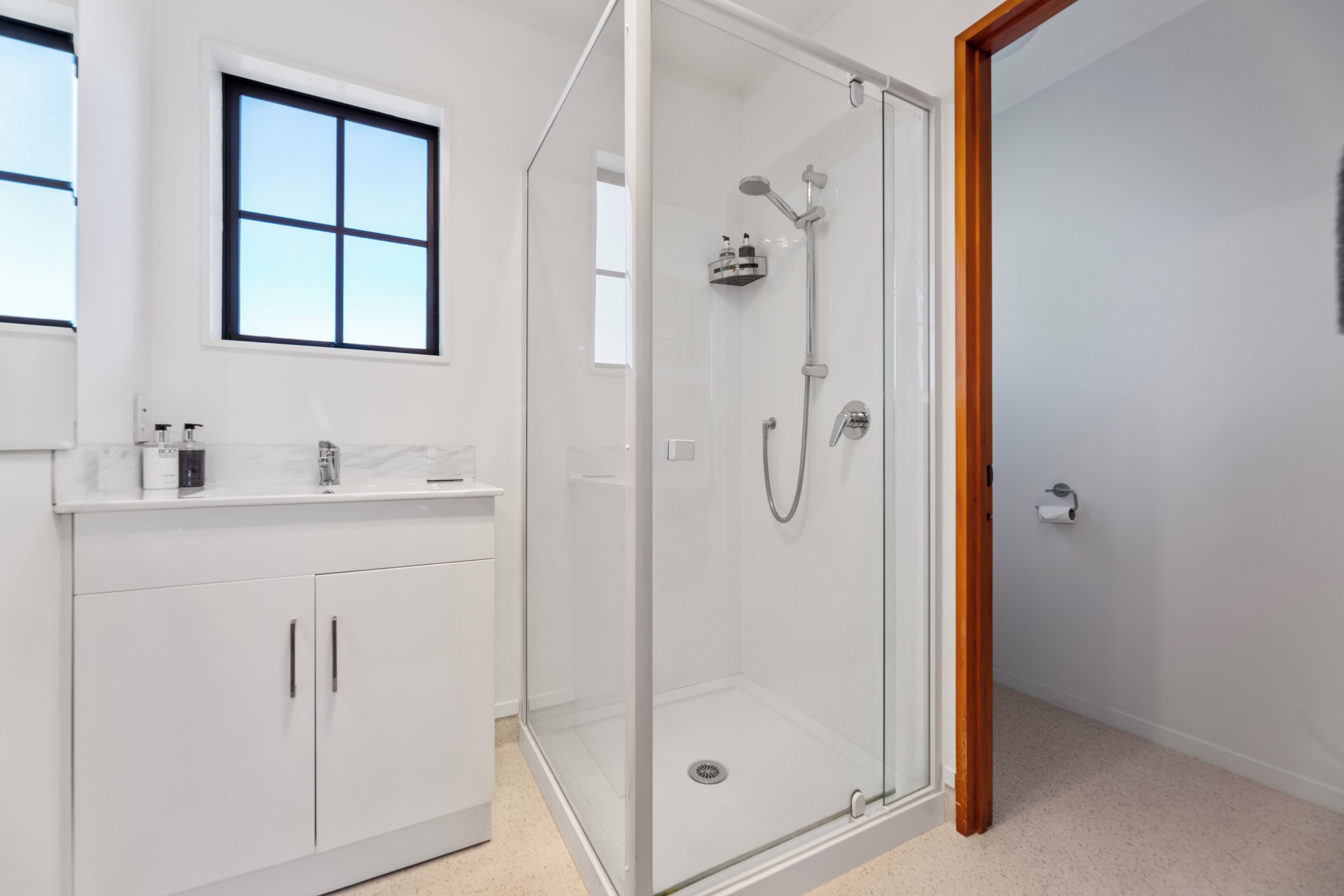 A modern bathroom with a glass-enclosed shower, a white vanity with a marble countertop, and a window above the sink.