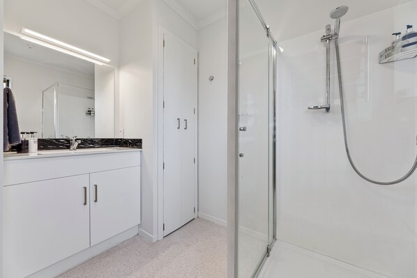 A modern bathroom with a glass-enclosed shower, white cabinetry, and a large mirror.