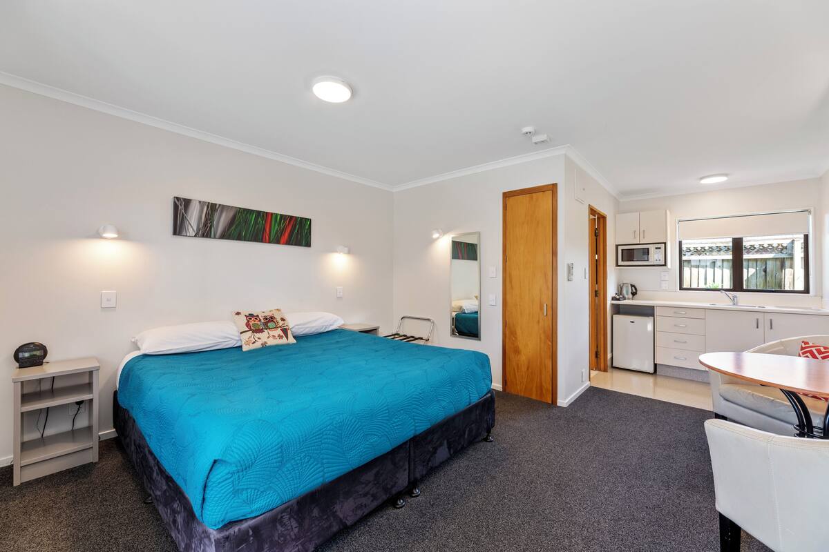 A bedroom with a bed, bedside table, and a view into the adjacent kitchen area.